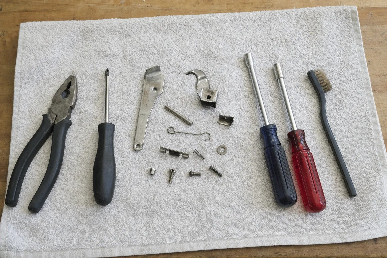 Pliers, a screwdriver and two nut drivers flanking a latch arm, a hooked catch, a thin spring, pins and a narrow brush